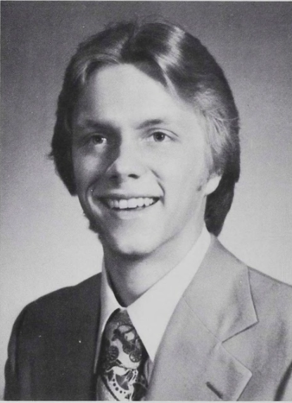 Old year book photo in black and white of a young man in suit and tie smiling at the camera.